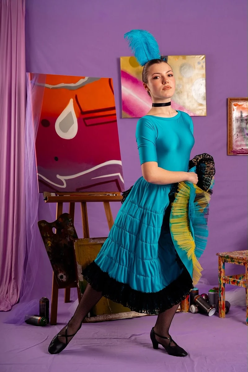 Ballerina in abito turchese con piume nei capelli davanti a una parete viola