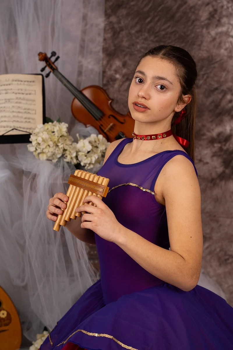 Giovane ballerina in body viola con il flauto di Pan, violino sullo sfondo