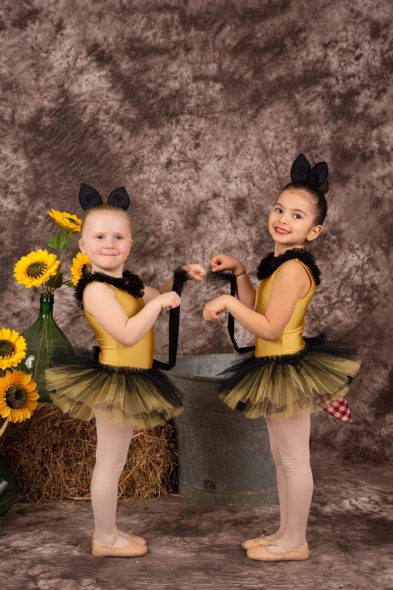 Due bambine in tutù giallo e nero con le orecchie da topolino, tra girasoli e paglia
