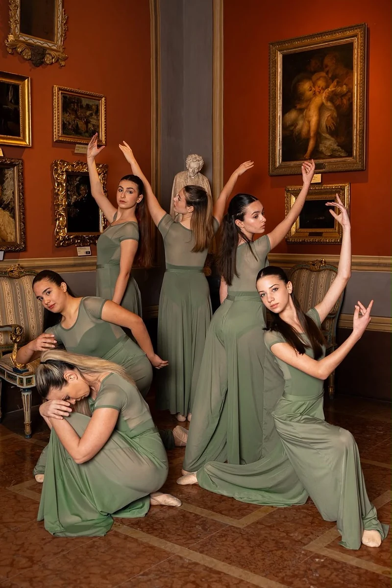 Gruppo di ballerine in abito verde in posa in una sala con quadri antichi