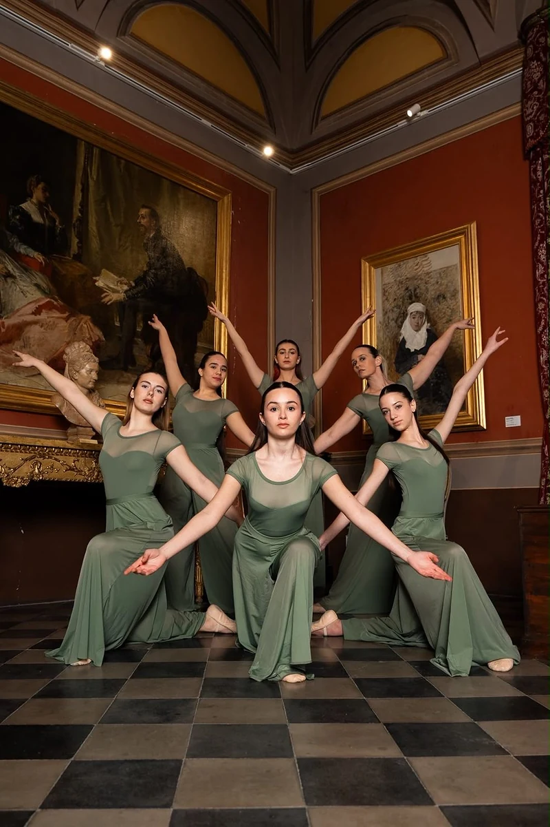 Ballerine in abito verde in posa simmetrica in una sala d'epoca con pavimento a scacchi