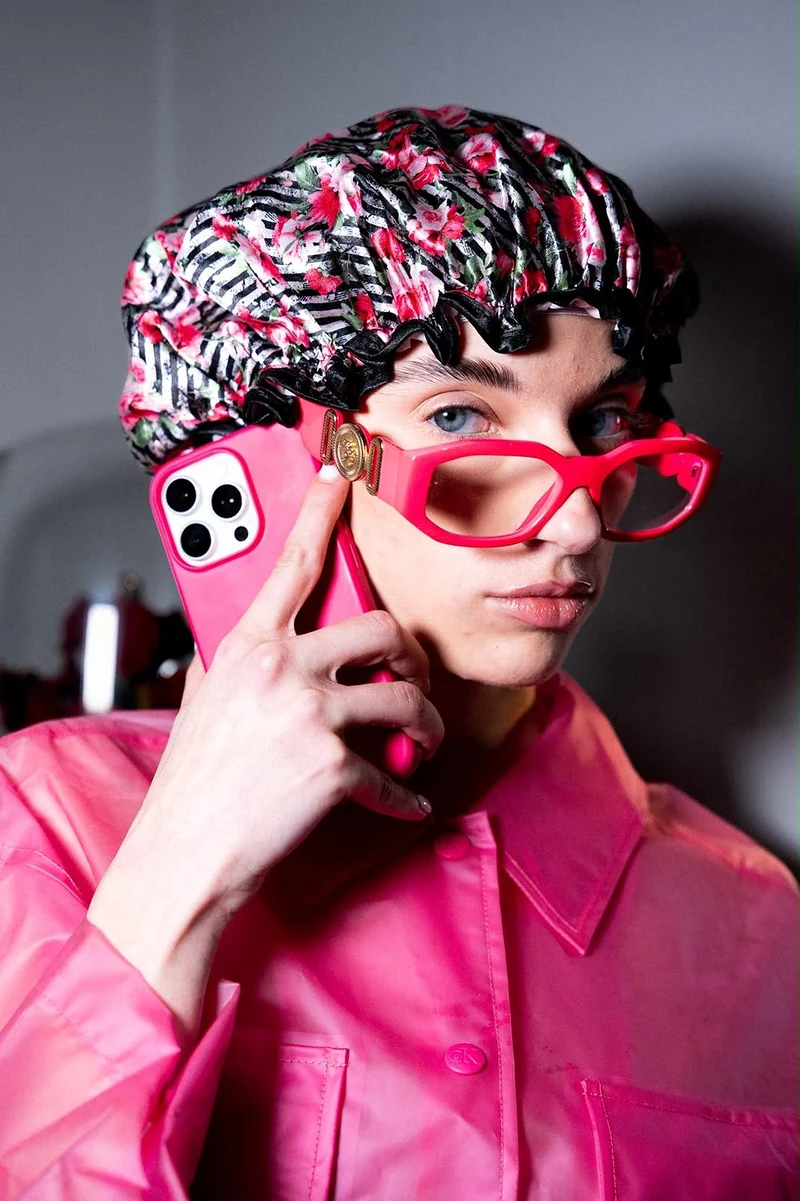 Ragazza con la cuffia da doccia e gli occhiali rosa che parla al telefono