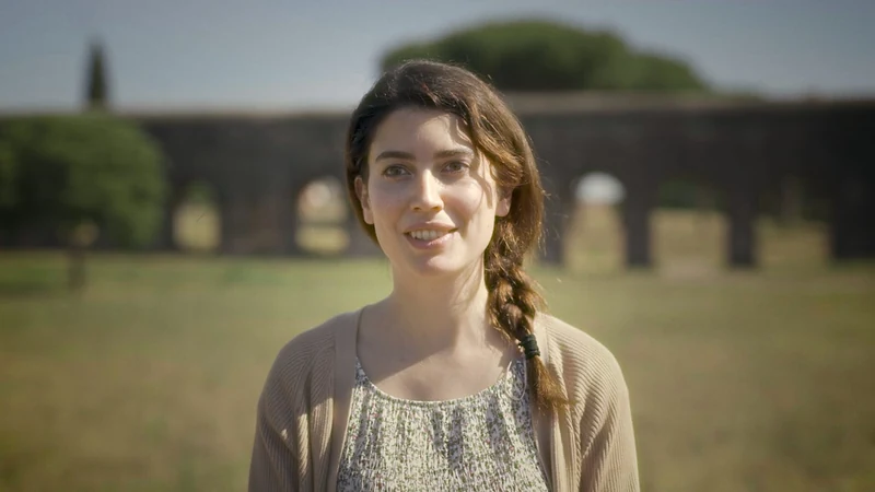 Ragazza con la treccia che sorride in un prato, acquedotto sullo sfondo