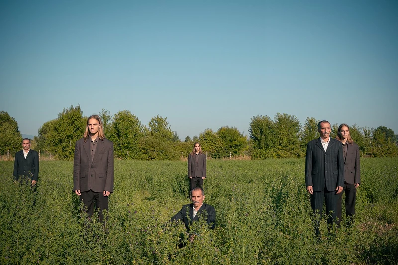 Editoriale: ragazzi in giacca scura in piedi in un prato verde sotto il cielo blu