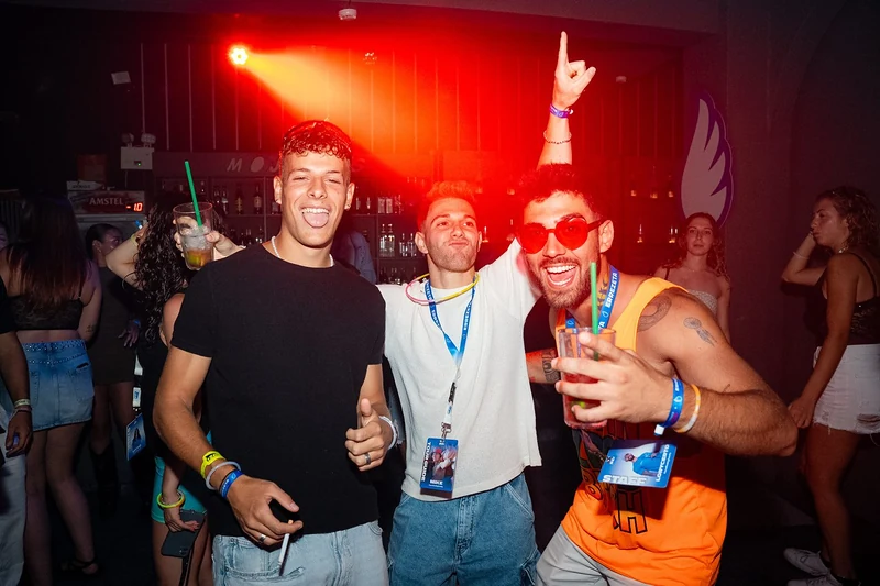 Festa in discoteca: tre ragazzi sorridenti sotto le luci rosse, uno con il braccio alzato