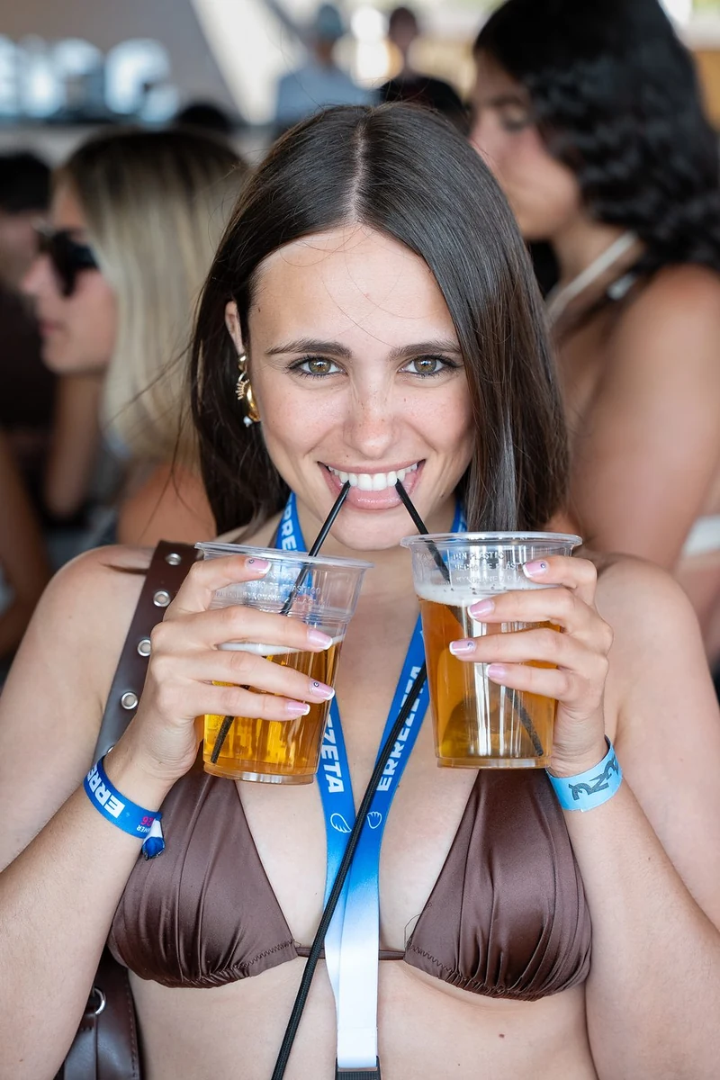 Ragazza sorridente con due bicchieri di birra e la cannuccia tra i denti