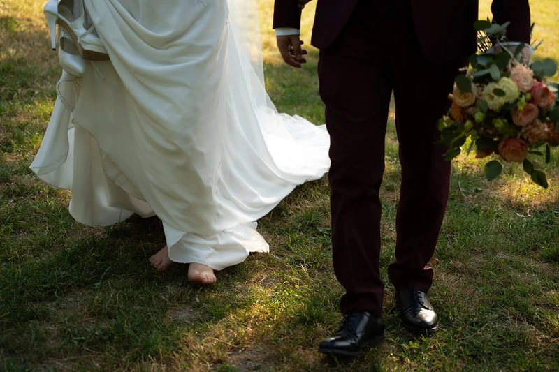 Sposi che camminano sul prato, lei a piedi nudi con l'abito sollevato, lui con il bouquet