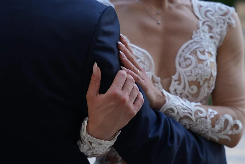 Mano della sposa con il pizzo della manica appoggiata sulla giacca blu dello sposo