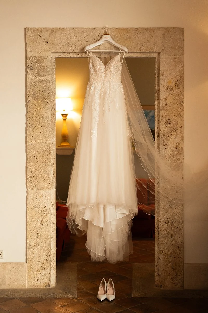 Abito da sposa con velo appeso in una porta di pietra, le scarpe a terra