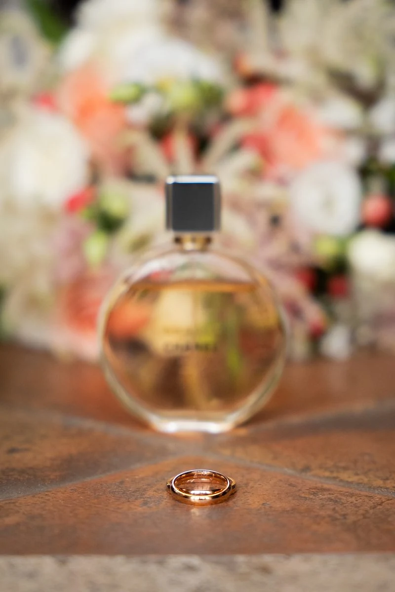 Fede nuziale accanto a una boccetta di profumo, bouquet sfocato sullo sfondo