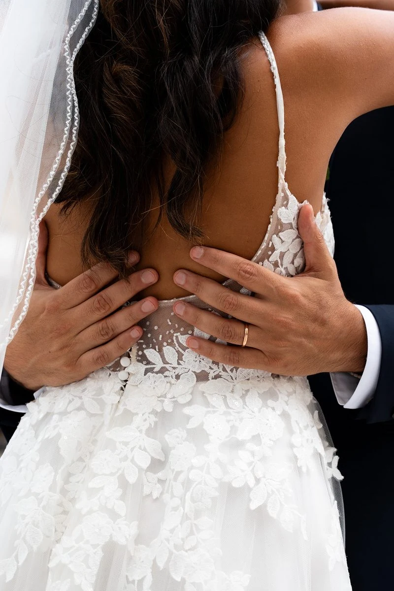 Sposo che abbraccia la sposa dalla schiena scoperta, abito di pizzo floreale