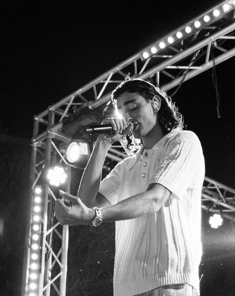Cantante in camicia bianca al microfono sotto le luci del palco, in bianco e nero