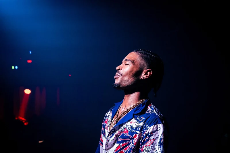Rapper di profilo con la camicia stampata illuminato da una luce blu