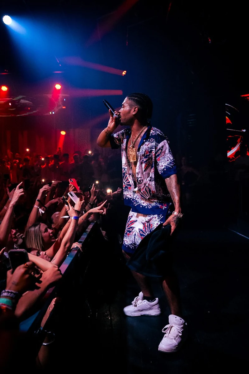 Rapper sul palco davanti al pubblico con le braccia alzate, luci rosse e blu