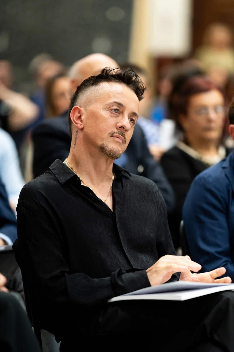 Uomo in camicia nera seduto tra il pubblico durante un concerto di musica classica