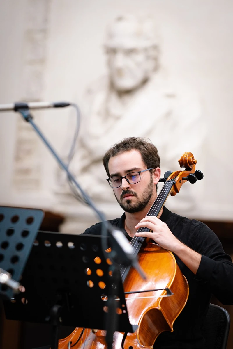 Violoncellista in primo piano davanti a un busto in marmo