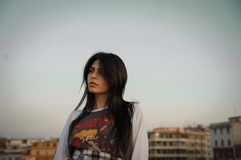 Ritratto di una ragazza dai capelli scuri al tramonto, con i tetti della città alle spalle