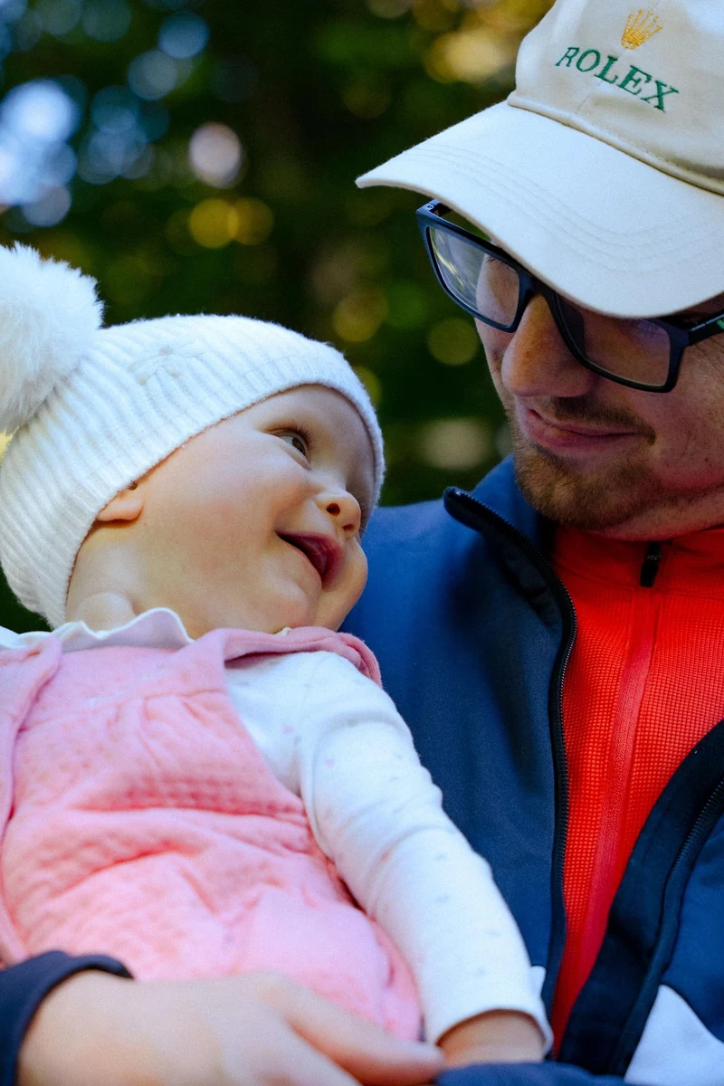 Papà con il cappellino che sorride alla sua bambina con la cuffia di lana