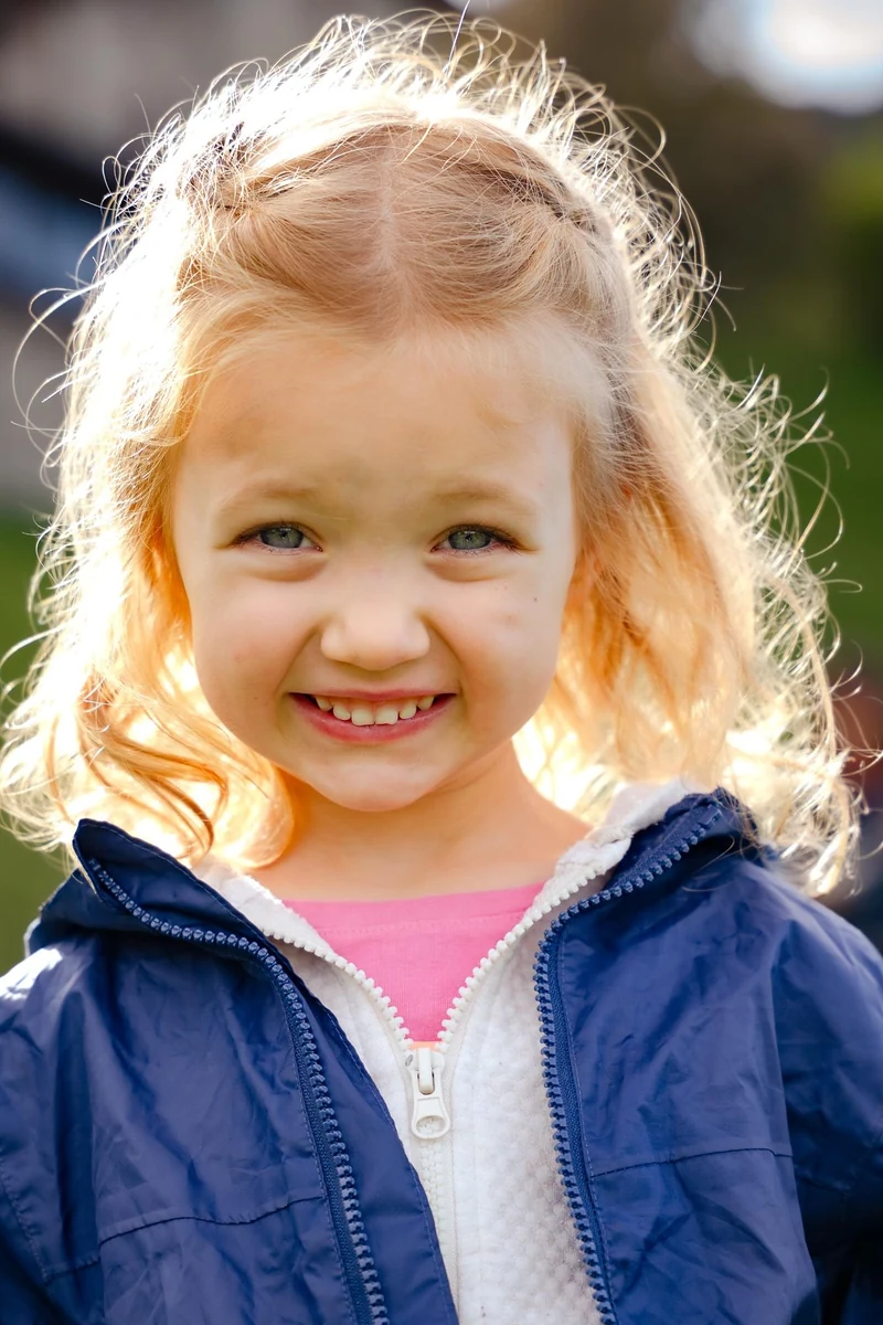 Primo piano di una bambina bionda sorridente in controluce
