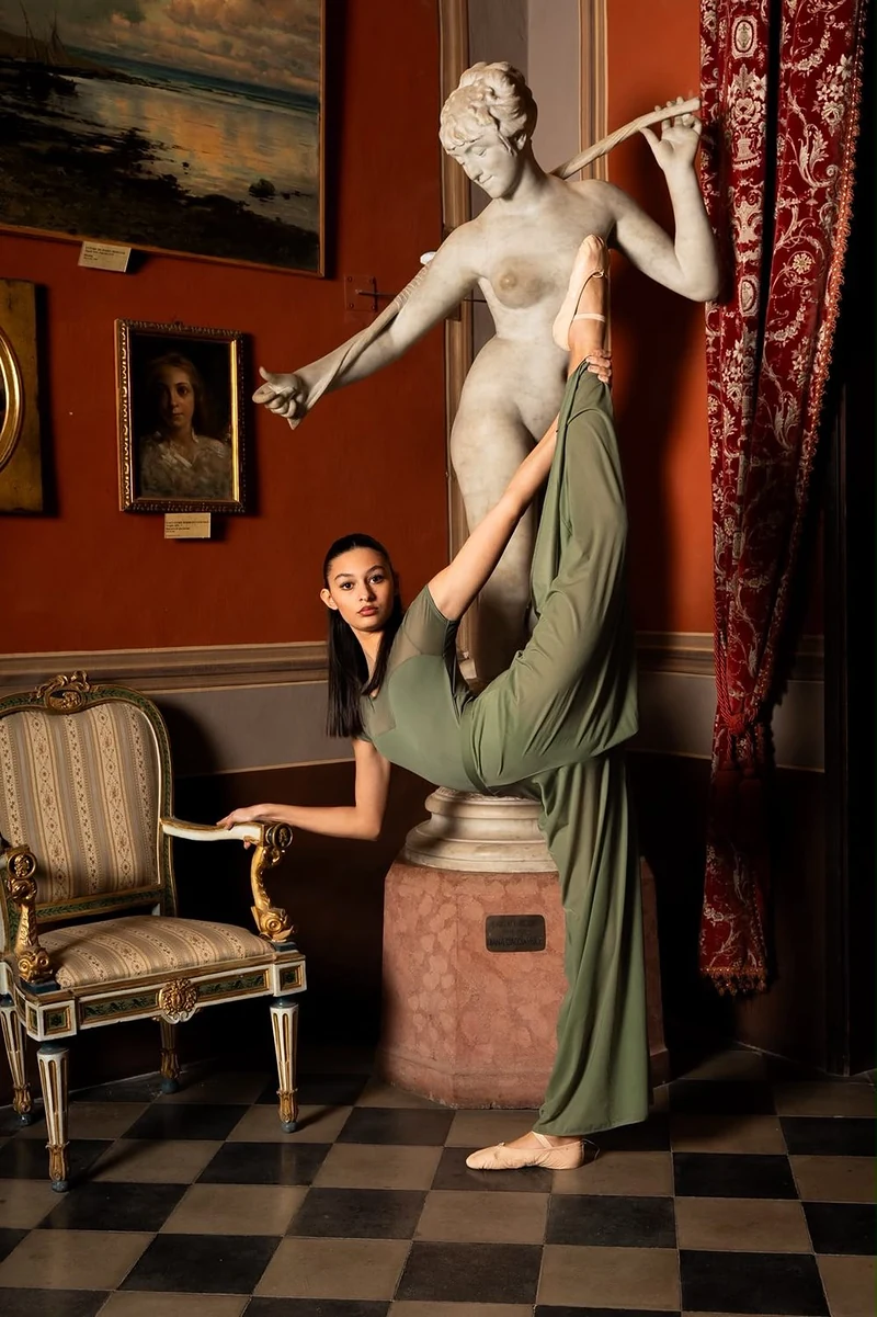Ballerina in abito verde con la gamba alzata contro una statua di marmo