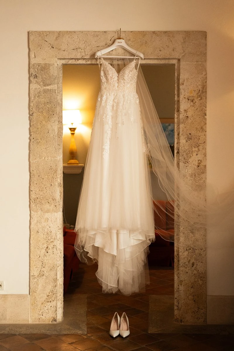 Abito da sposa con velo appeso in una porta di pietra